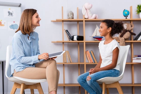 Smiling african american child looking at psychologist with digital tablet during consultation with blurred office on background